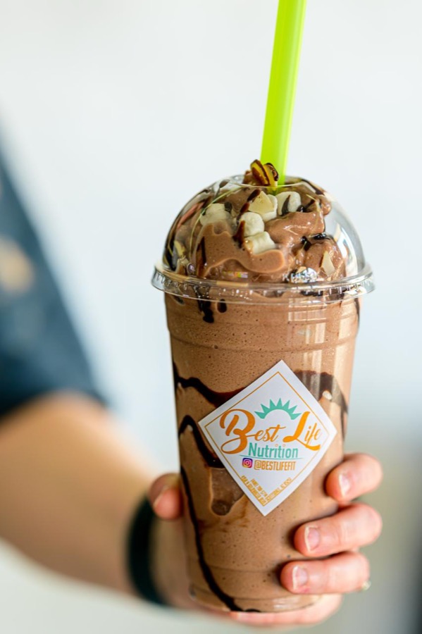 A hand holding a chocolate smoothie from Best Life Nutrition